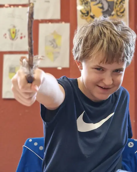 Zauberschüler mit selbst gebautem Zauberstab vor den Wappen der Häuser