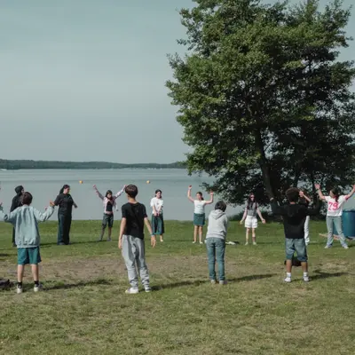 A class spread out by the lake, doing a group warm-up exercise together