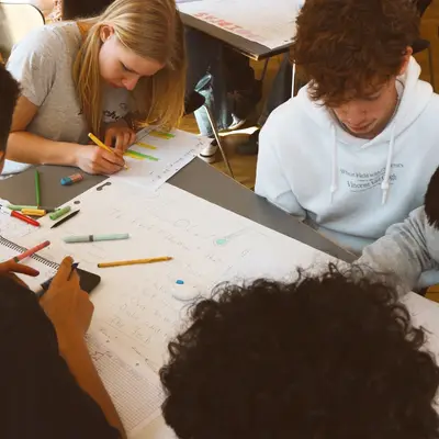 Students working in small groups on a workshop task, markers and flip-chart paper spread across the table