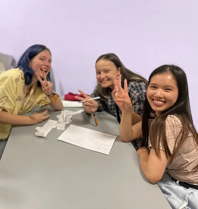 Drei Schülerinnen arbeiten lachend an einem Tisch an einer Workshop-Aufgabe